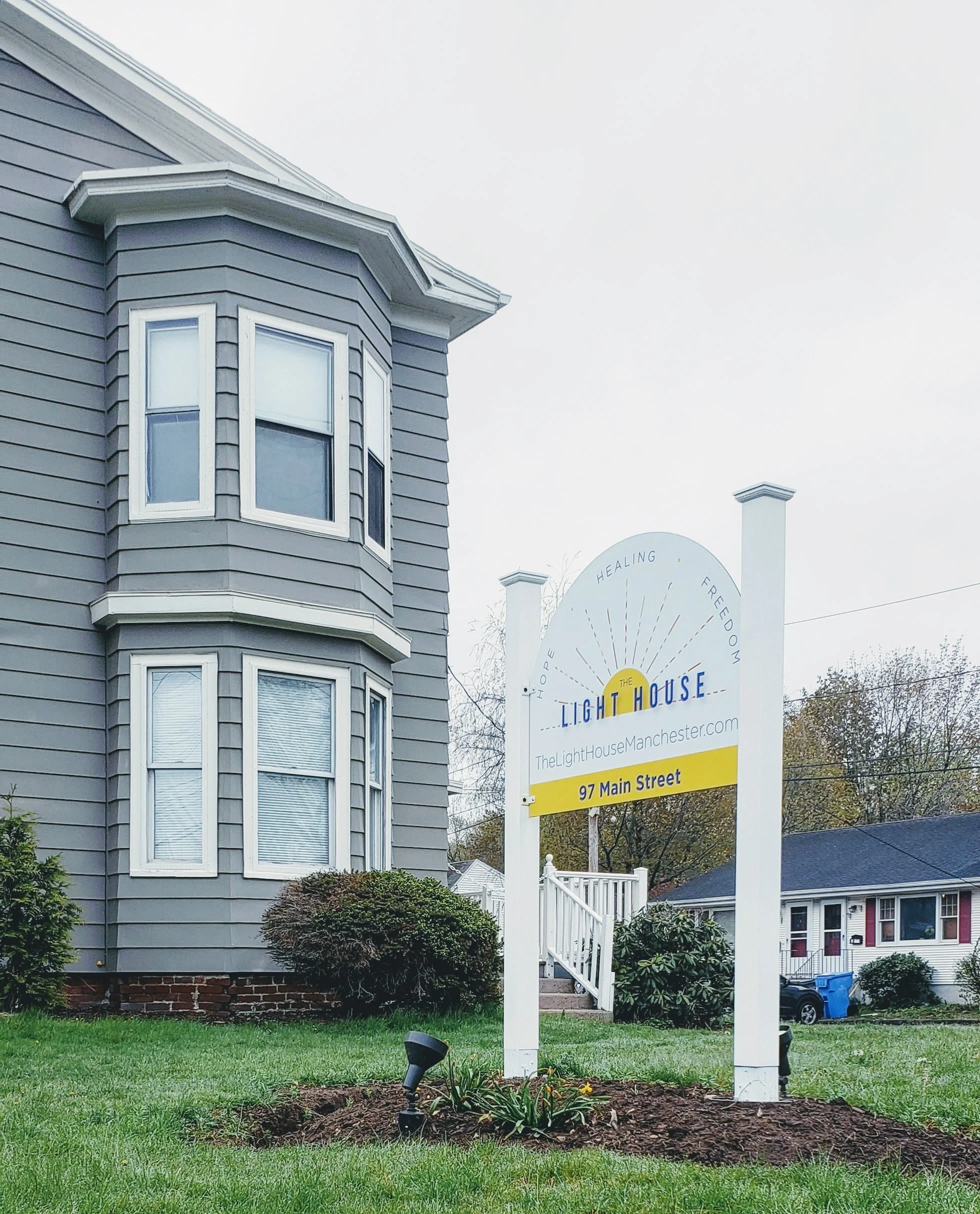 A house and a sign for The Light House Manchester, with a lawn and landscaping in the front.