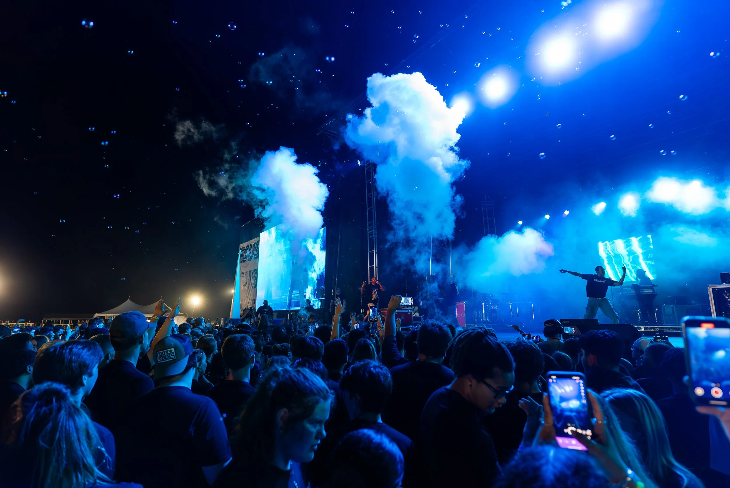 Crowd at a music concert standing on a stage with bright blue lights and smoke.