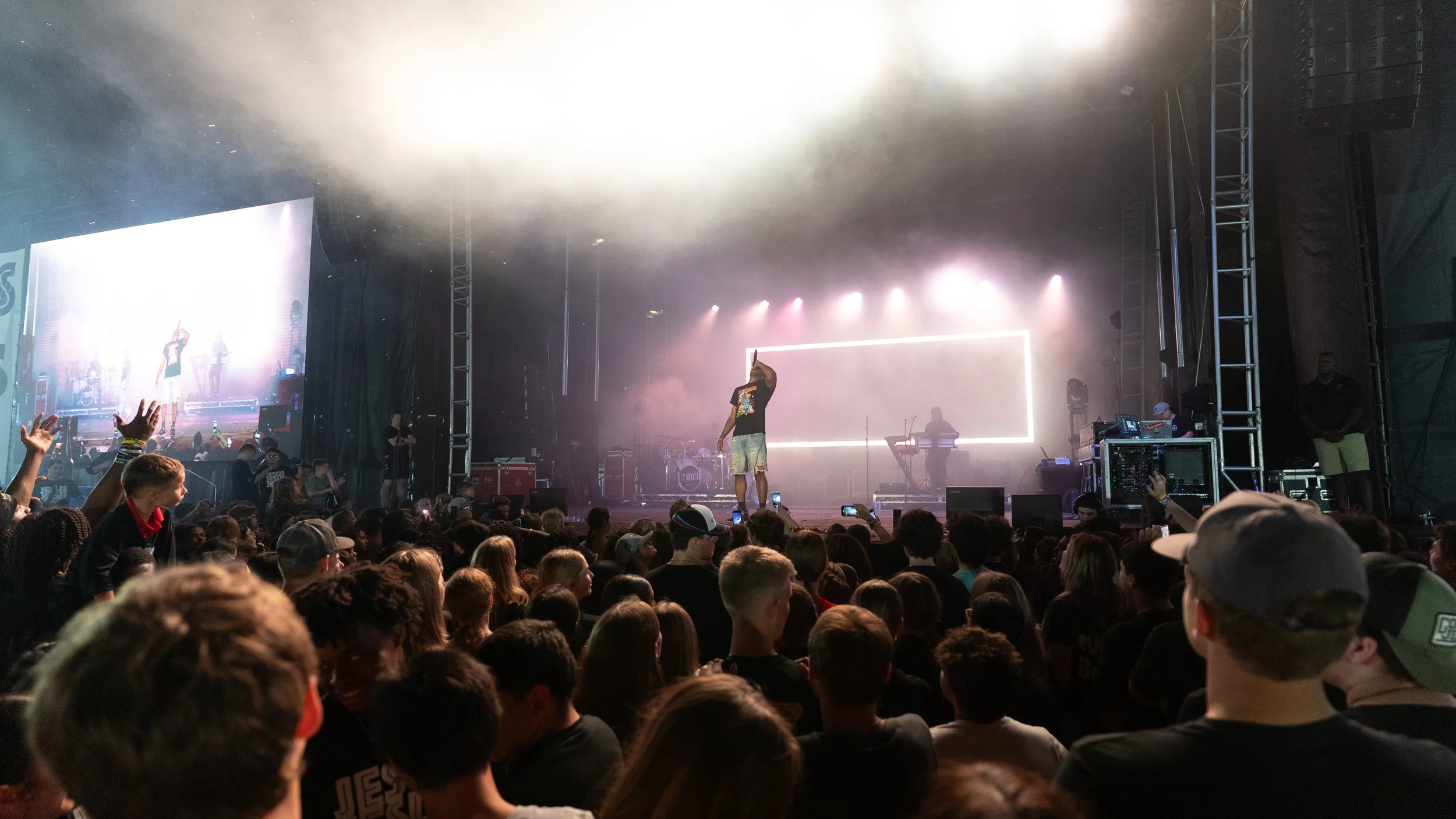 A concert scene with a large audience facing a stage where a performer is singing. The stage has bright lights and musical equipment, with some operation controls visible on the right side.