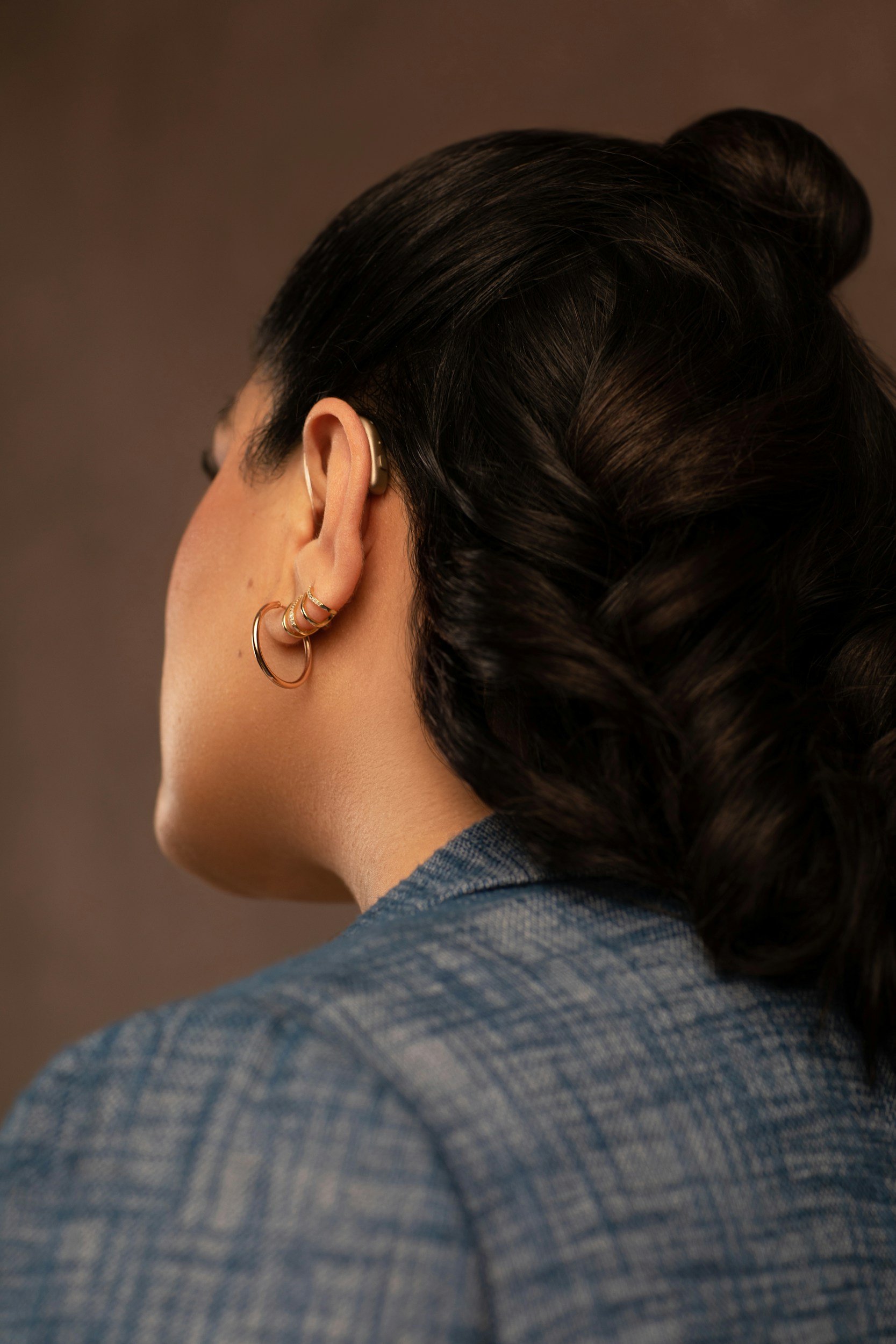Close-up of a woman's head turned sideways, showing her black hair styled in vintage waves with earrings and a blazer.
