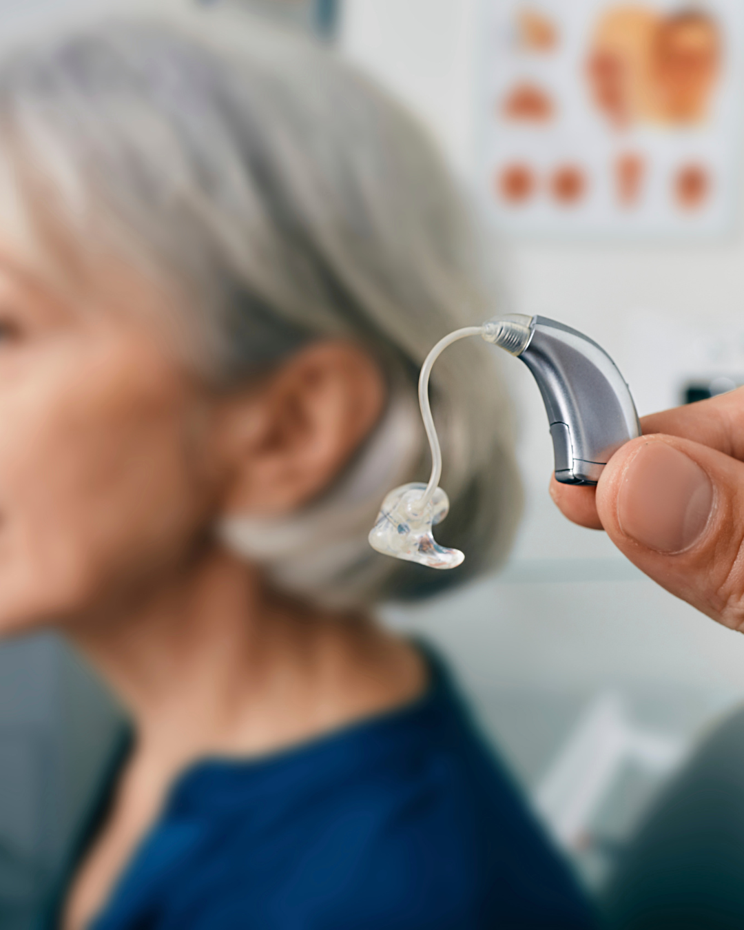 A person with gray hair wearing a face mask is fitted with a hearing aid.