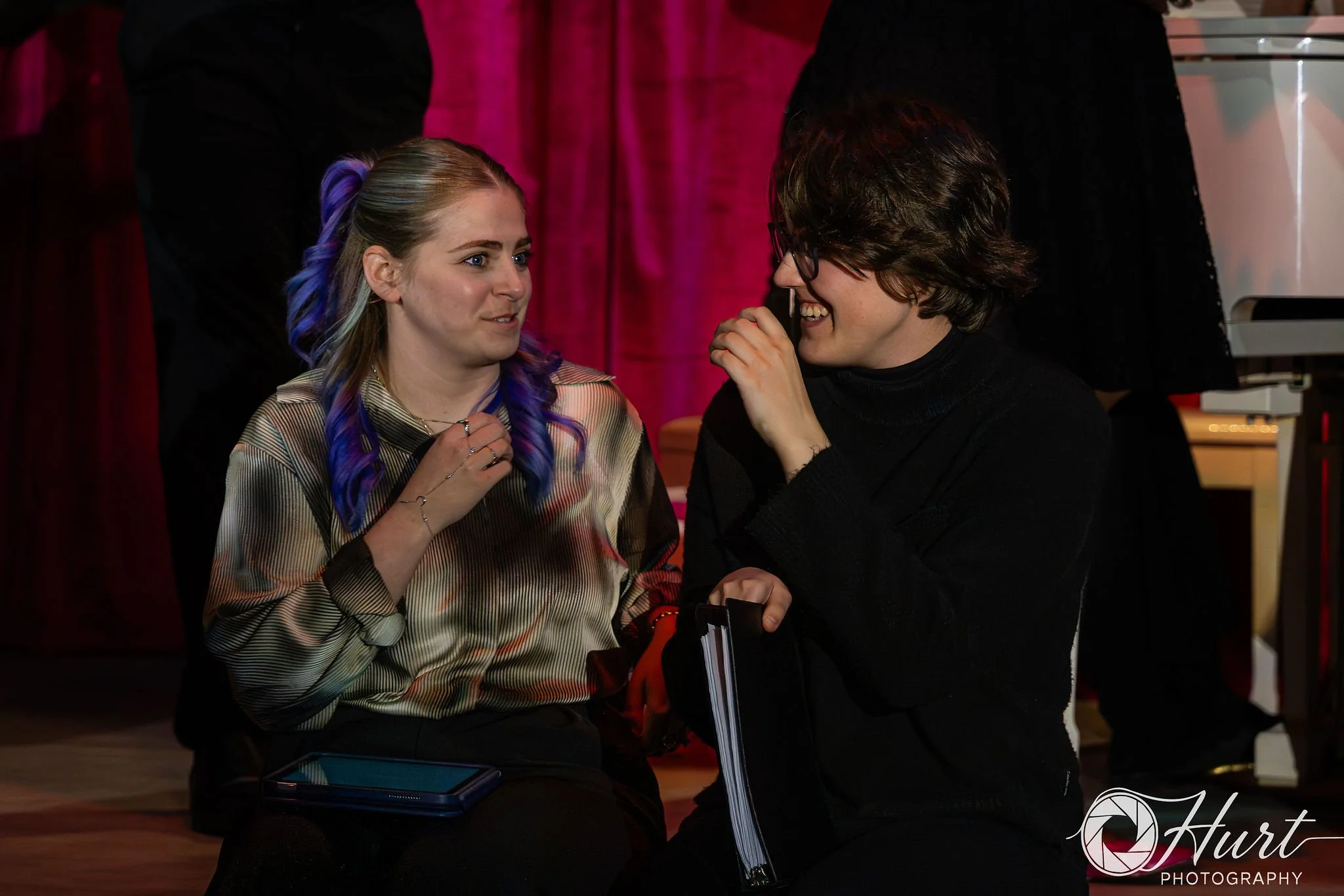 Two performers sit on the edge of the stage engaged in song and storytelling. 