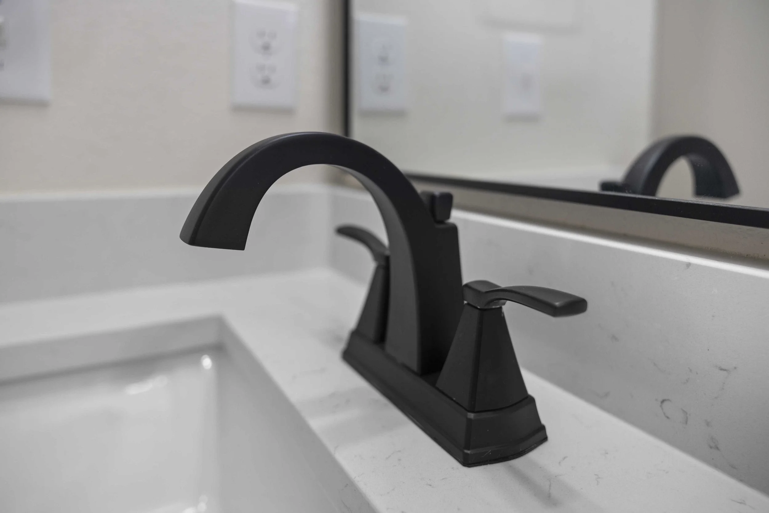 Close-up of a black bathroom sink faucet with a mirror reflecting the faucet and a white countertop.