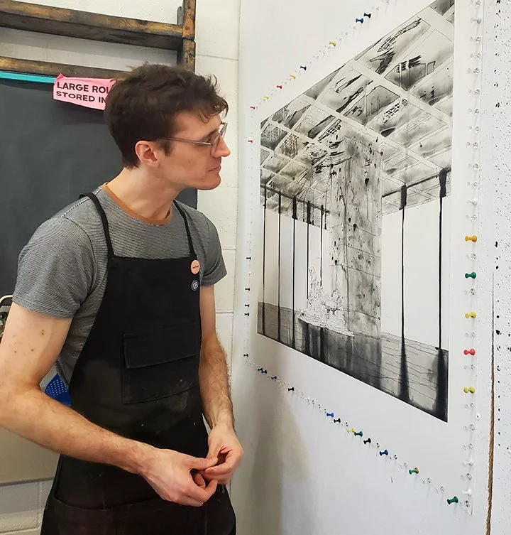 Person looking at a large black-and-white etching print pinned to a wall, with colourful pushpins around the edges.