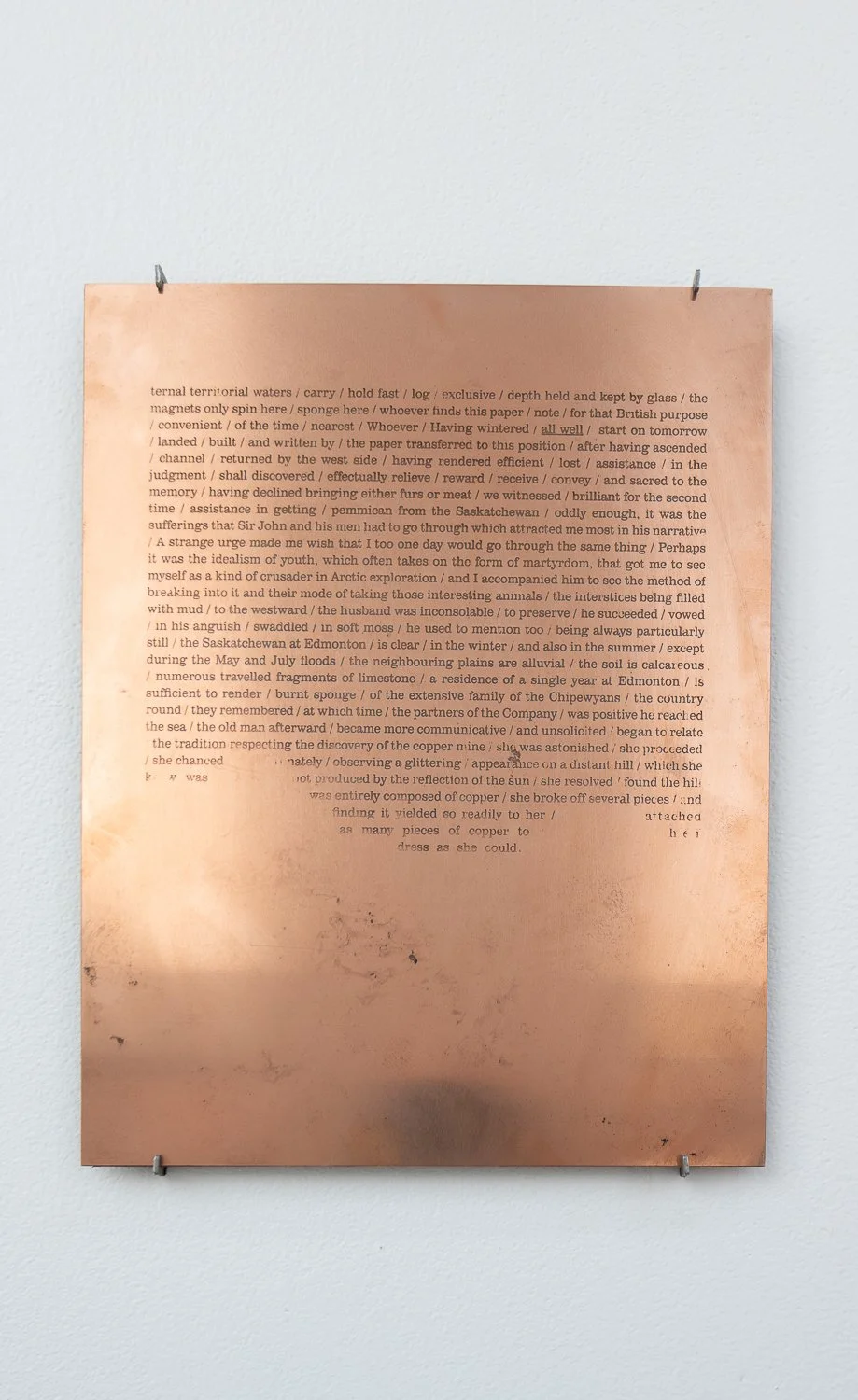 A copper plate mounted on a white wall with text engraved on it.