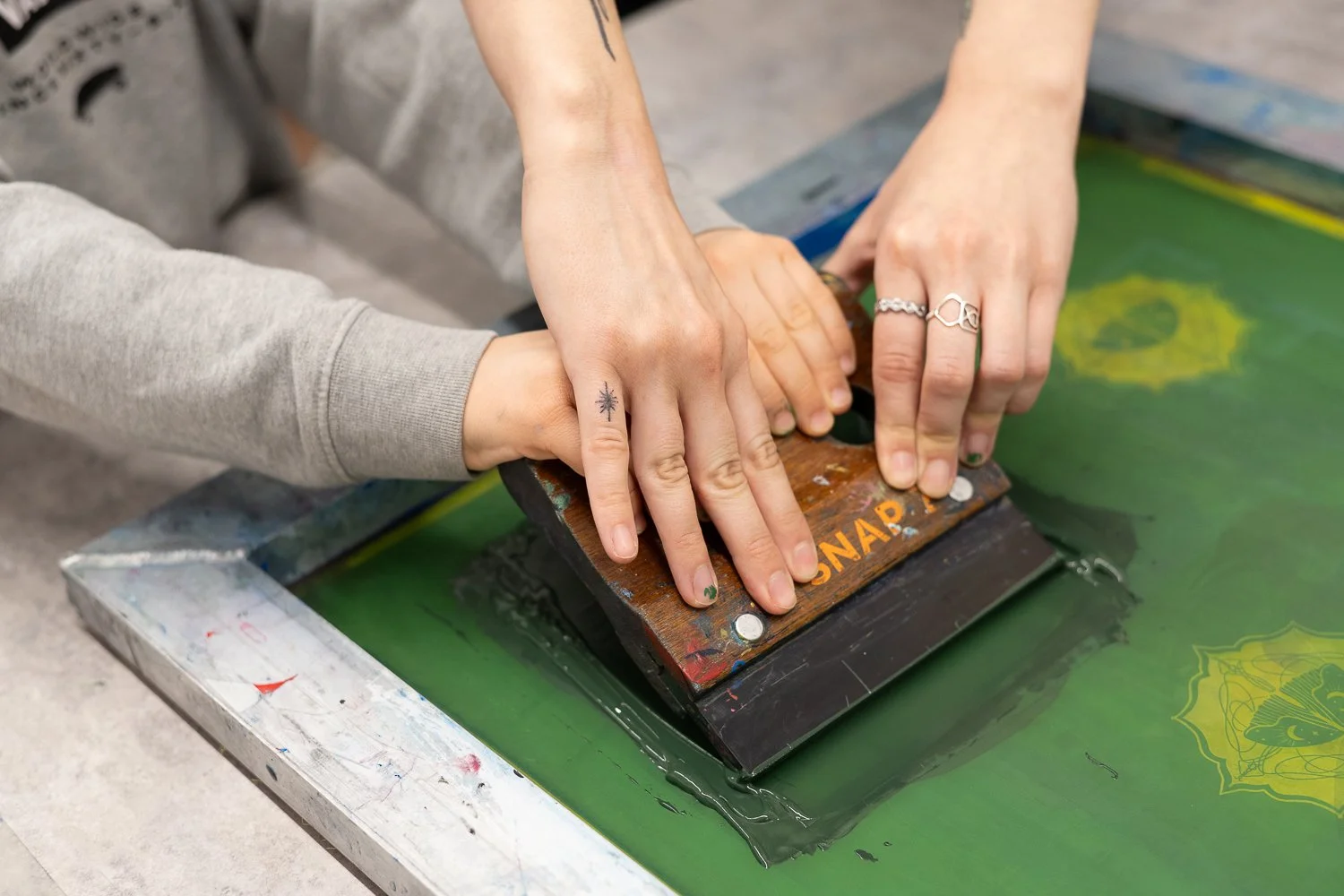 Two people pressing a handprint onto a green surface using a brayer in a printmaking process.