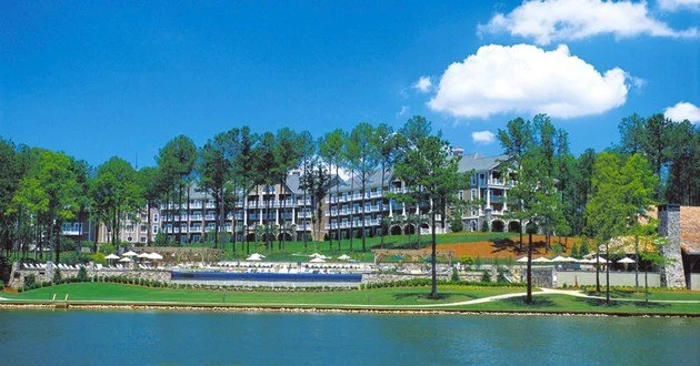 Luxury waterfront residential complex with trees, a lake, and a clear blue sky.
