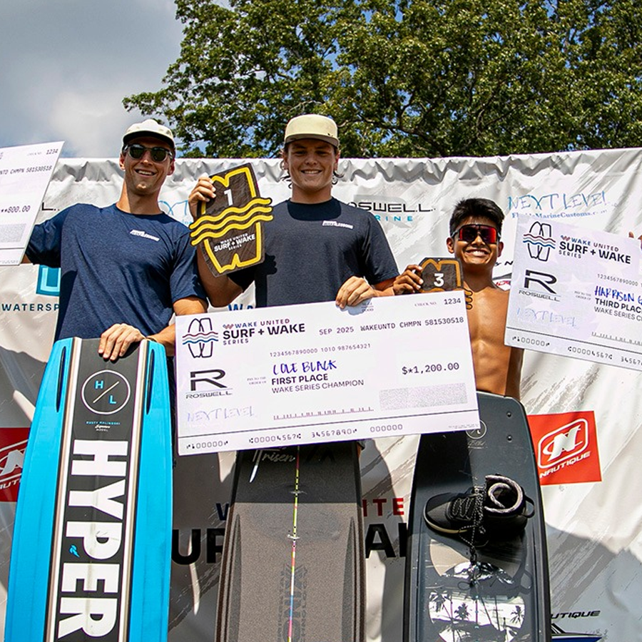 Three young male surfers are standing on a podium during an award ceremony, holding large checks and a surfboard with surfing gear, celebrating their victory in a surfing competition.