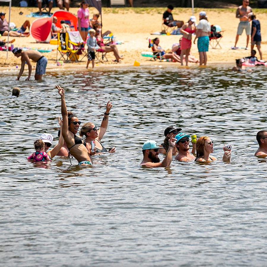 People swimming and relaxing at a beach, with others sitting on chairs and children playing on the sand.