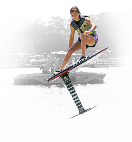 Young girl wakeboarding on a lake with boats in the background.