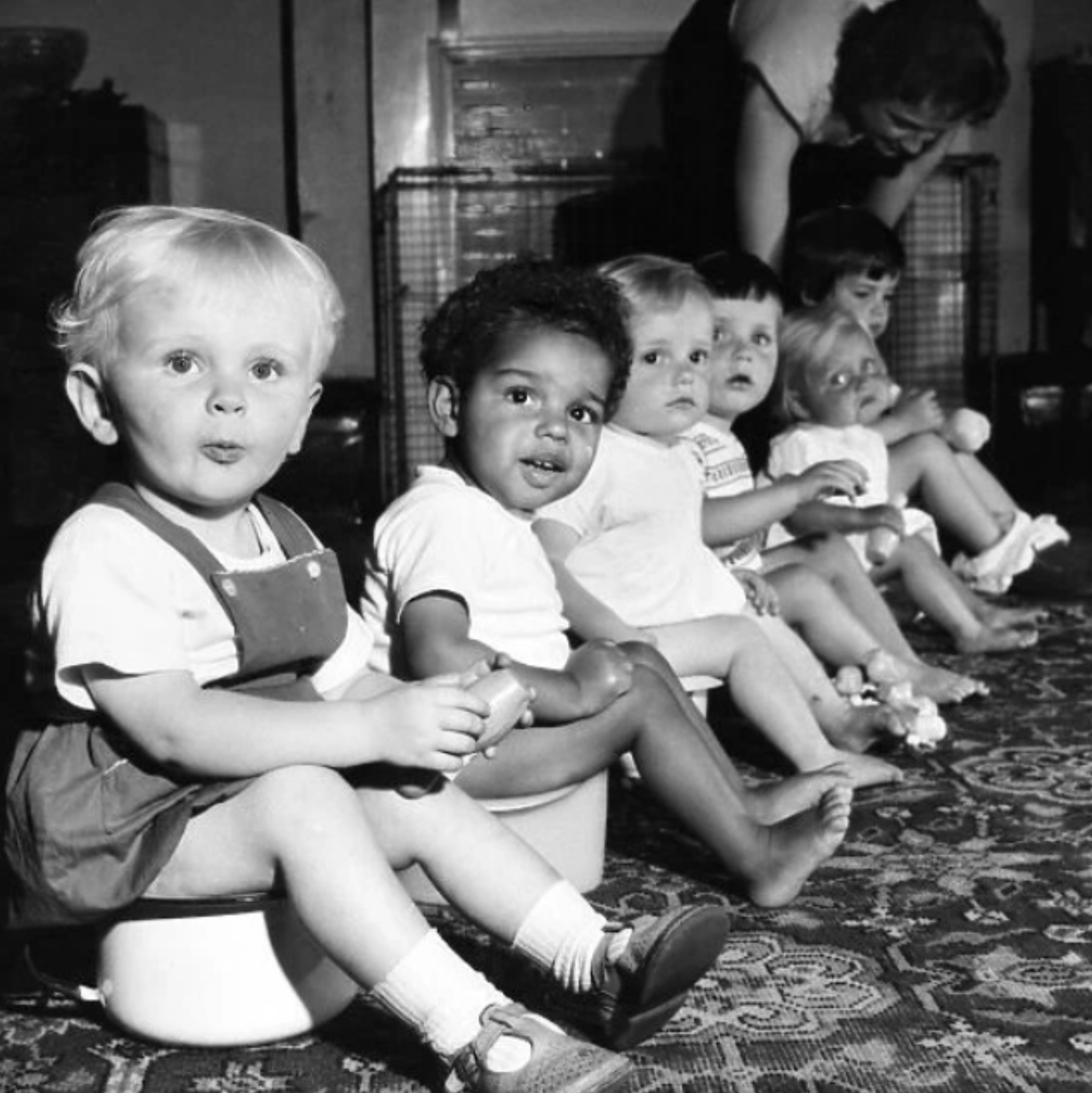Black and white photo of young children all sitting on potties for toilet time.