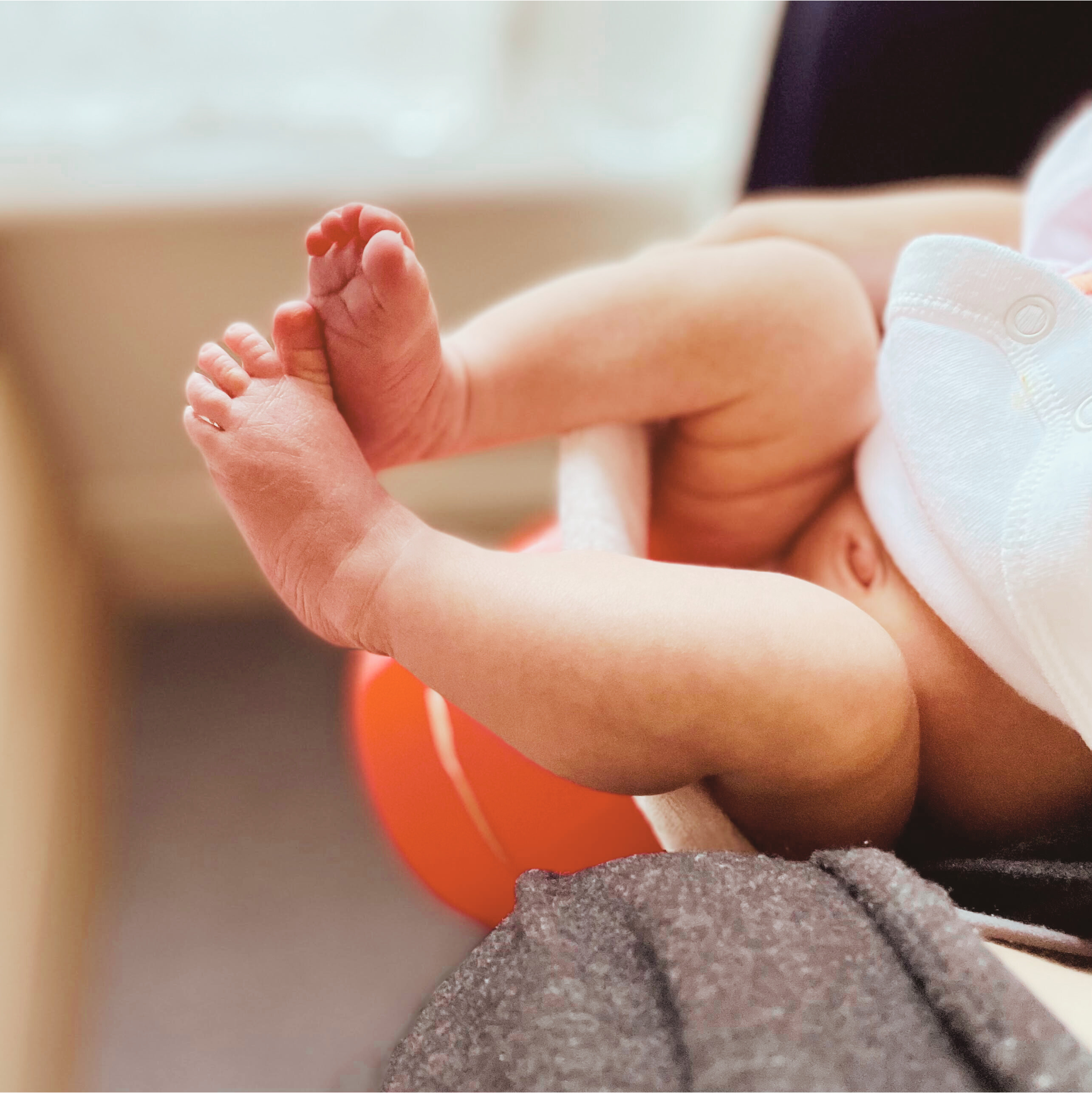 Close-up of a newborn baby's foot being gently held by an adult whilst baby is sitting on a tophat potty.