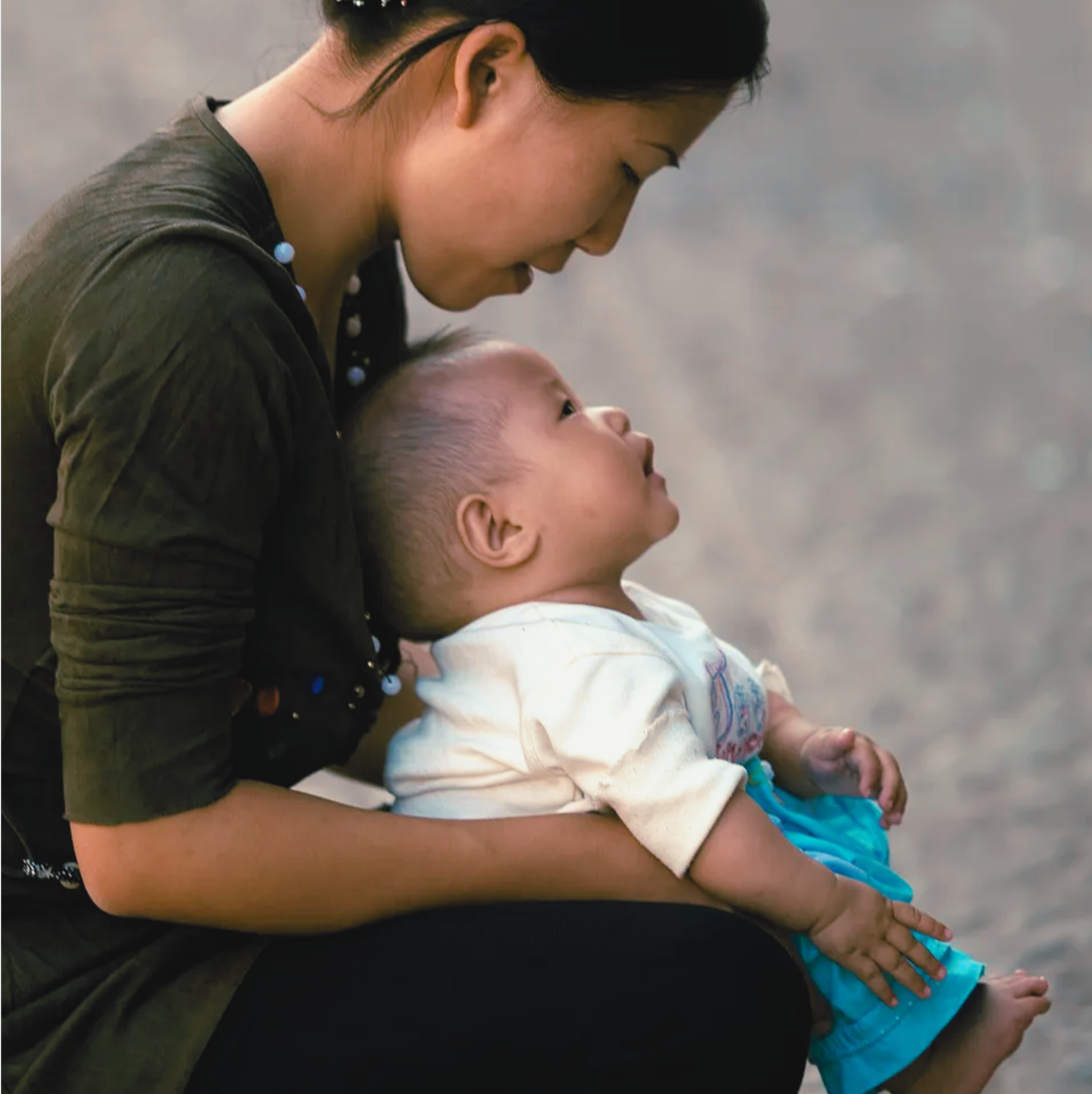 An asian woman bending down pottying her young baby outdoors.