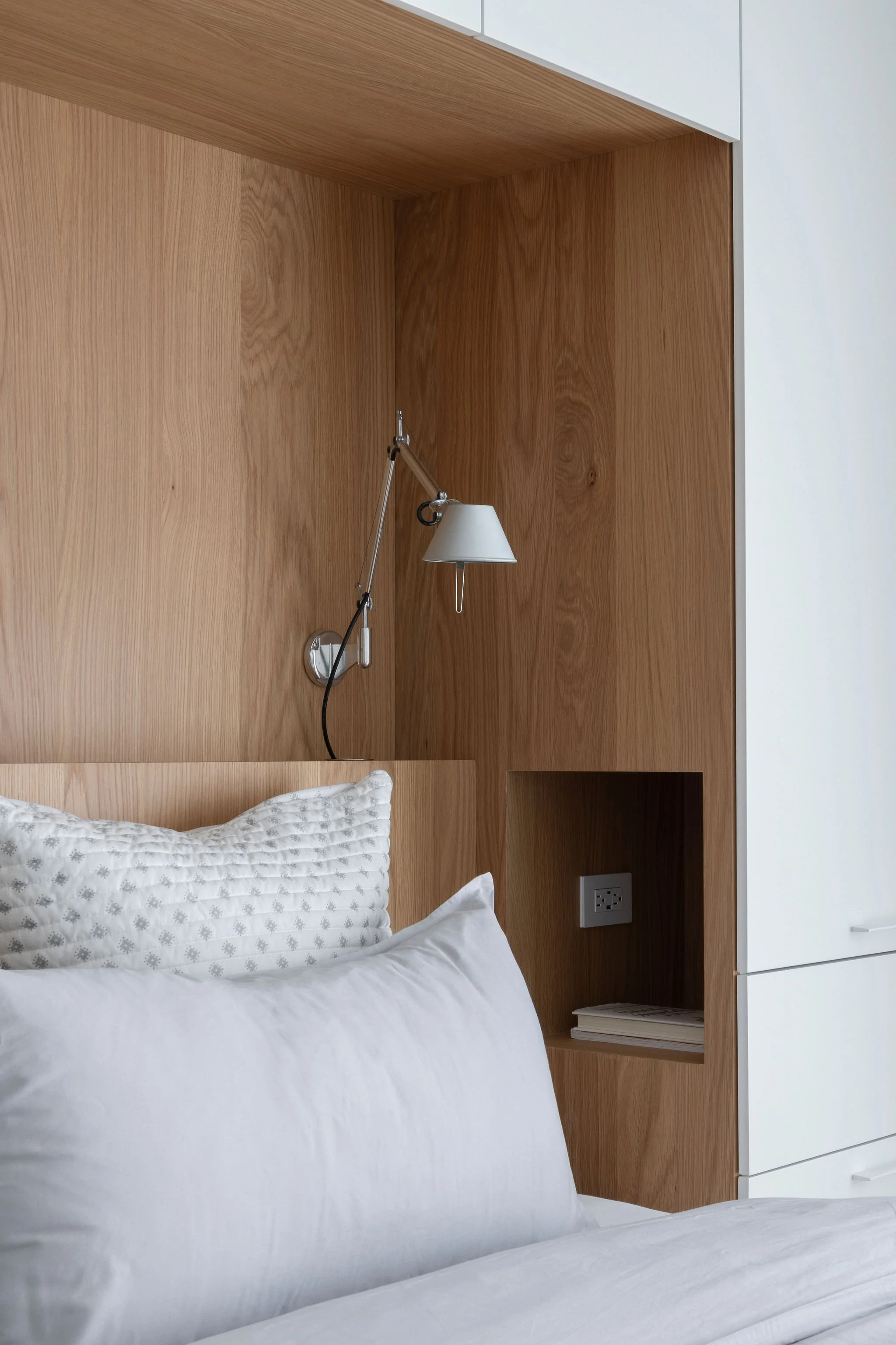 L'intérieur d'une chambre avec tête de lit en bois, oreillers blancs et une lampe de lecture fixée au mur.