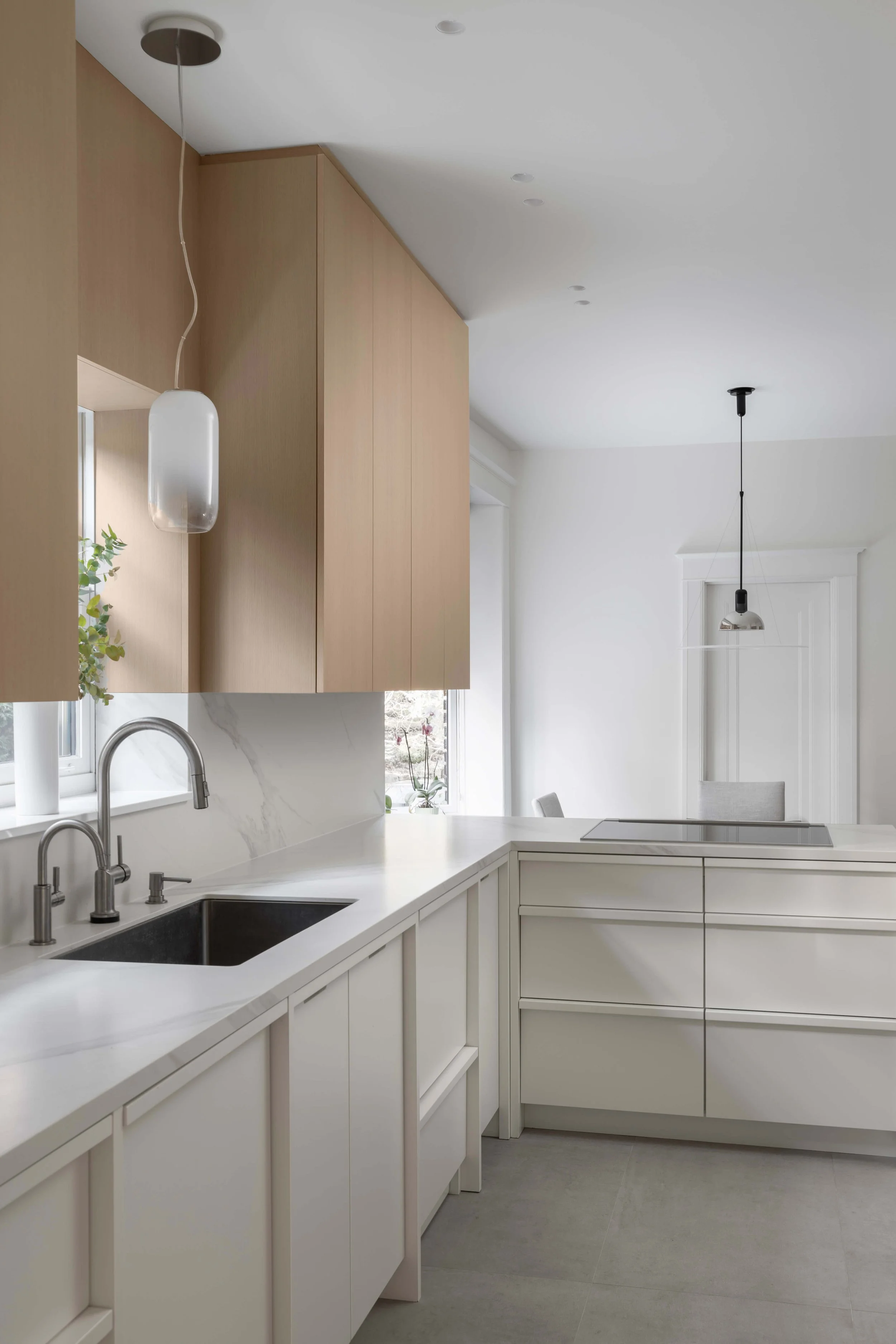 Cuisine moderne avec comptoirs blancs, armoires en bois clair, lavabo double et éclairage suspendu