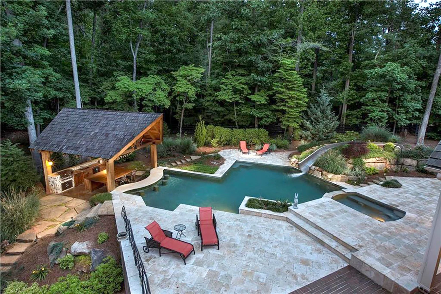 Backyard with swimming pool, hot tub, slide, lounge chairs, covered patio, trees, and landscaped garden.