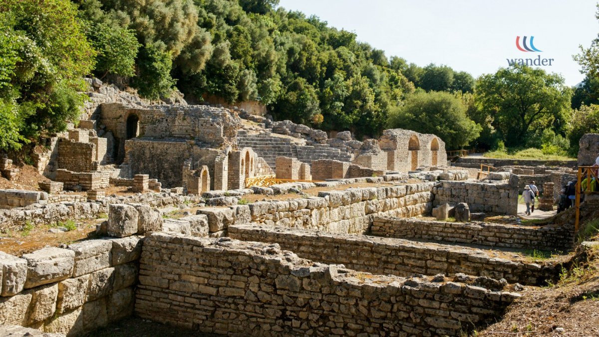 Ancient ruins with stone walls and arches surrounded by green trees and a clear sky.