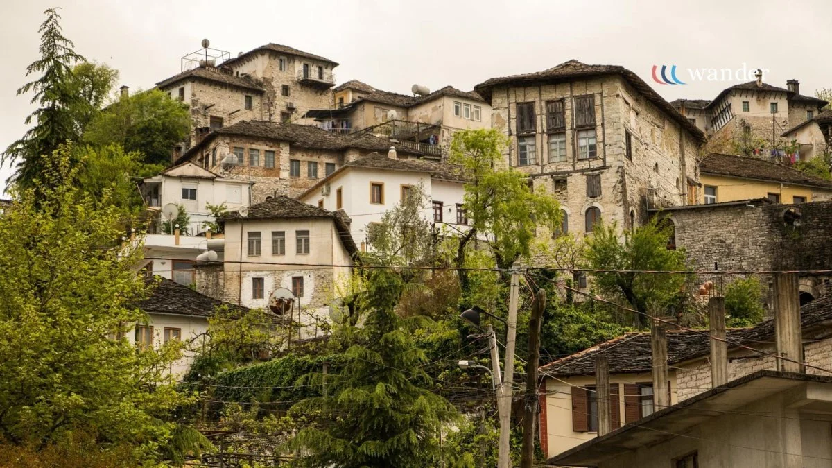 A hillside with multiple old stone and wooden houses, surrounded by green trees and overcast sky.