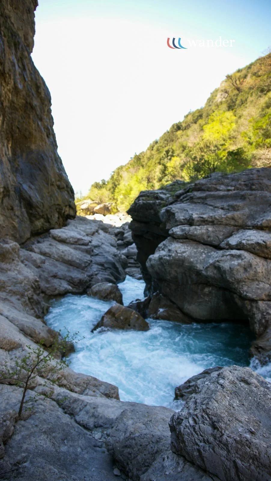 A narrow river flowing through a rocky canyon with green trees on the hillside in the background.