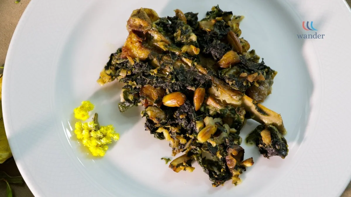 A serving of savory green leafy vegetable casserole with seeds, garnished with yellow flowers, on a white plate.