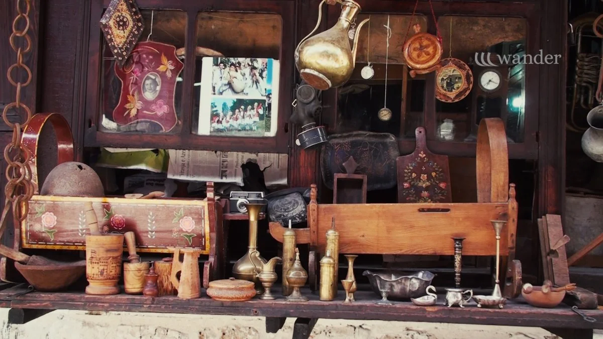 Collection of vintage and antique objects, including wooden and metallic items, a photo frame with a picture, a camera, and various utensils on a wooden shelf.