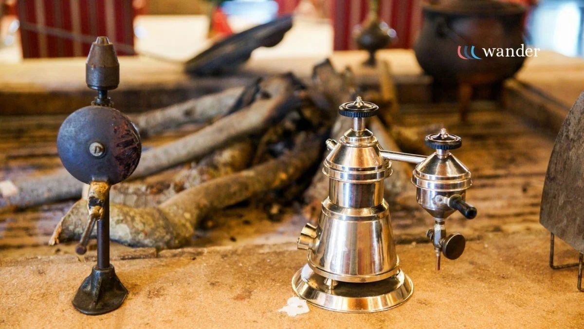 A vintage sniper rifle with a wooden stock and scope is displayed on a table made of rustic wood, behind a metal pepper grinder, on a wooden surface, with pottery in the background.