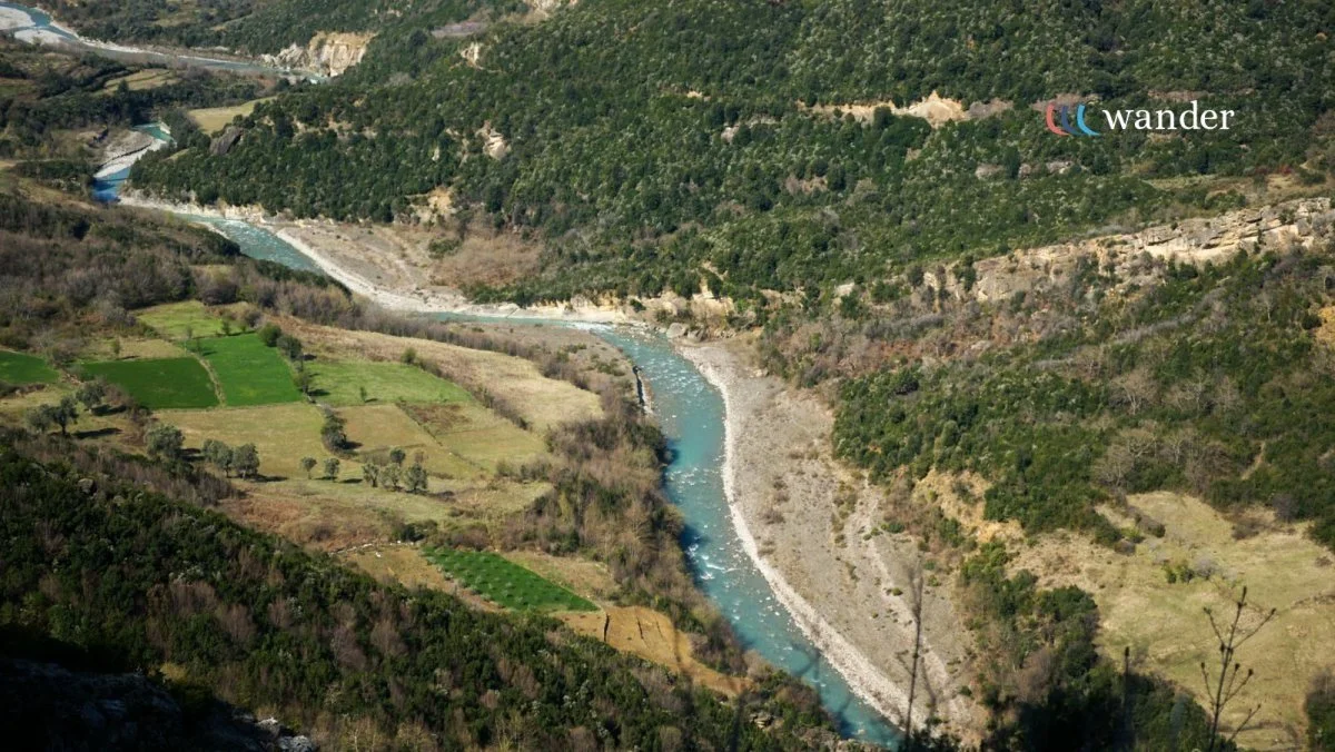 Aerial view of a winding river flowing through a valley surrounded by green hills and patches of farmland.