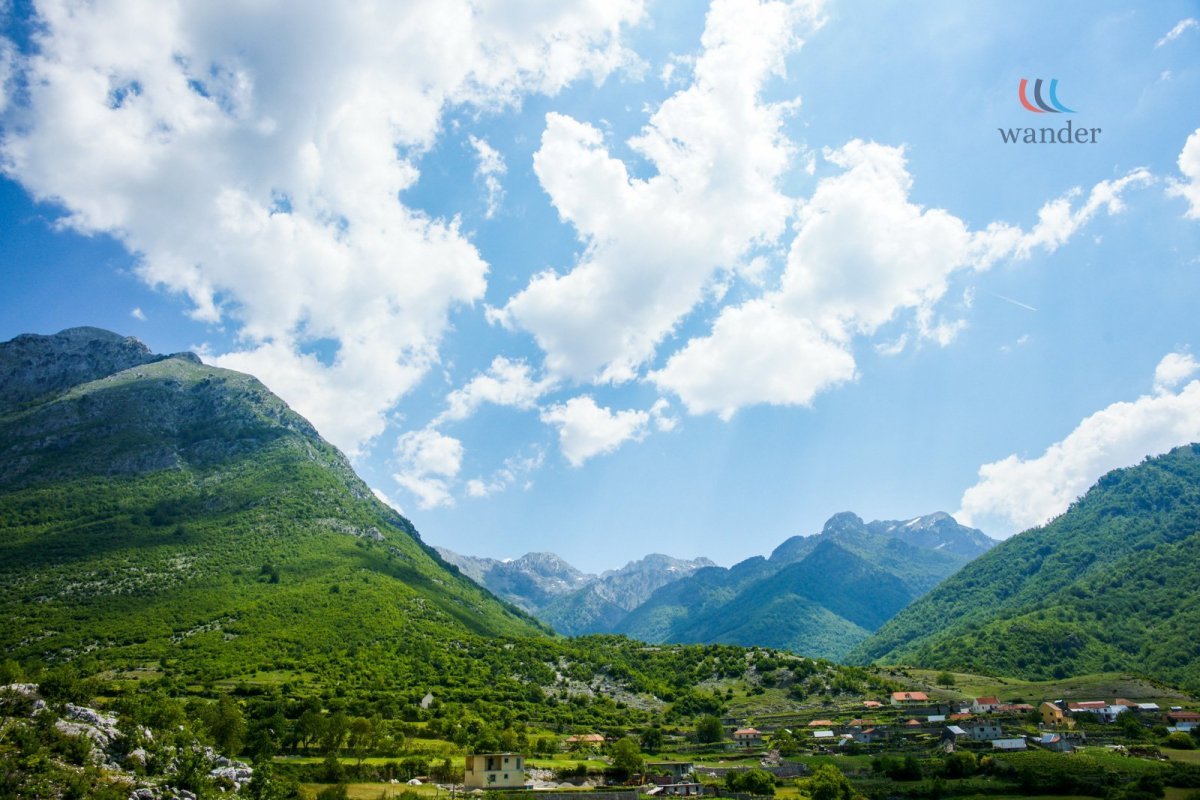 A scenic view of green mountains underneath a partly cloudy blue sky, with small houses at the foothills.
