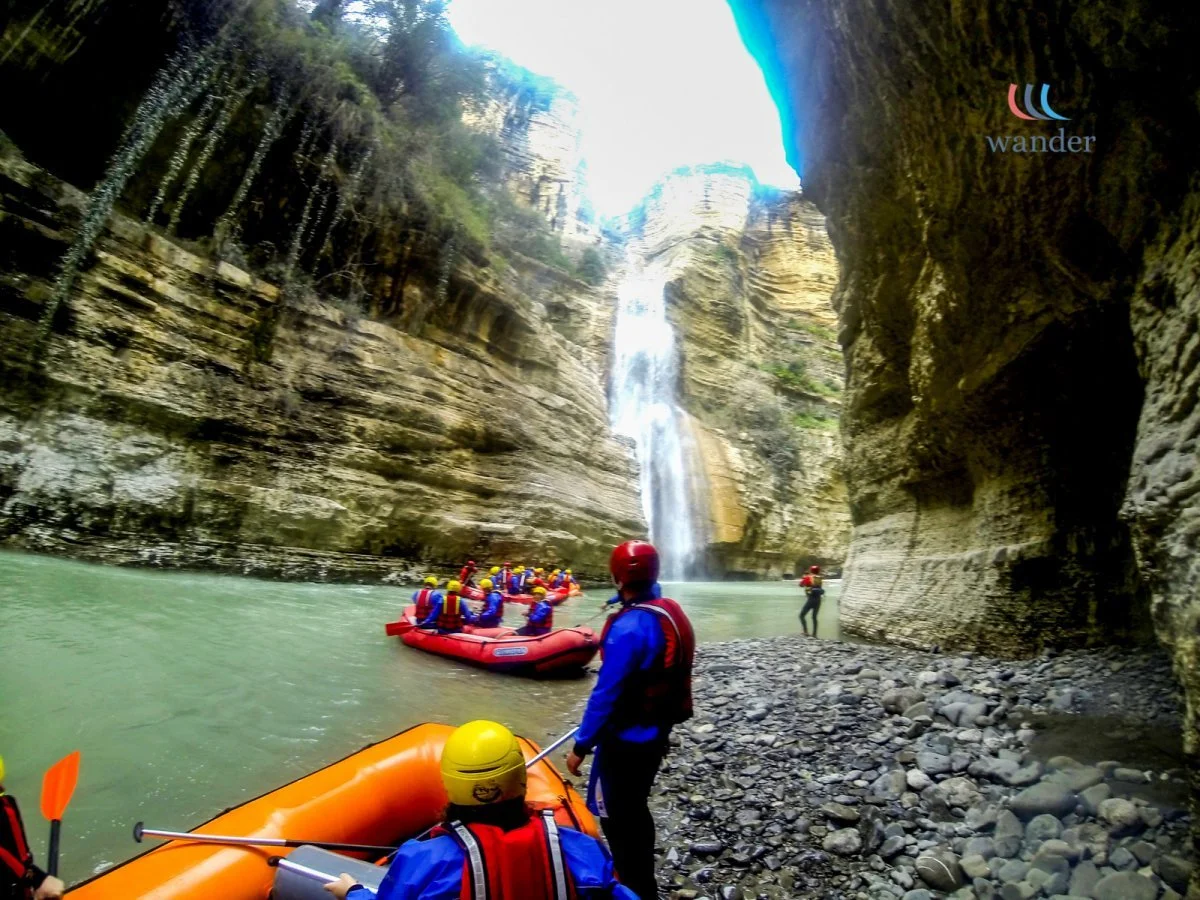 People on a rafting adventure near a waterfall in a canyon with steep rocky walls.