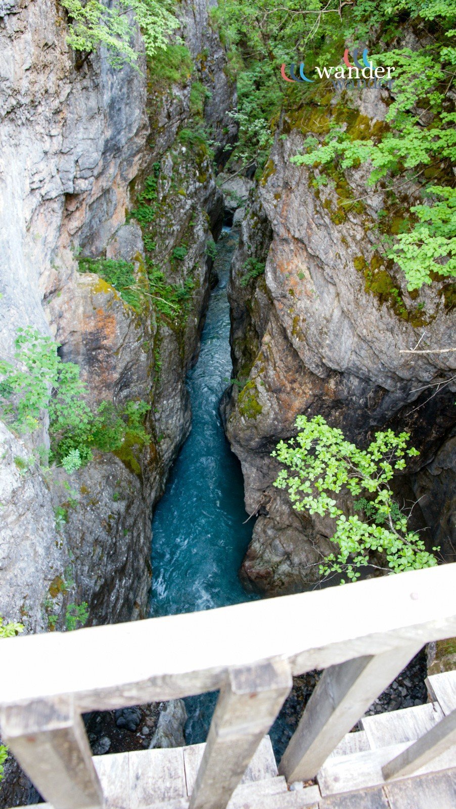 View from a bridge showing a narrow canyon with steep rocky walls and a flowing blue river in the middle, surrounded by green foliage.