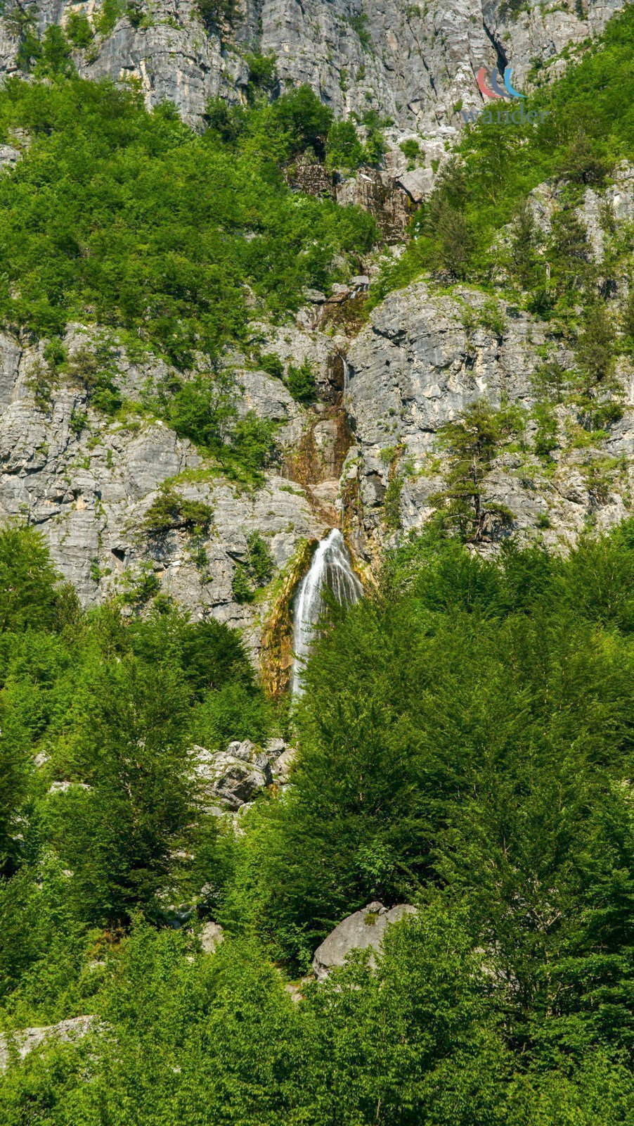 A tall waterfall cascading down a rocky mountain surrounded by lush green trees.