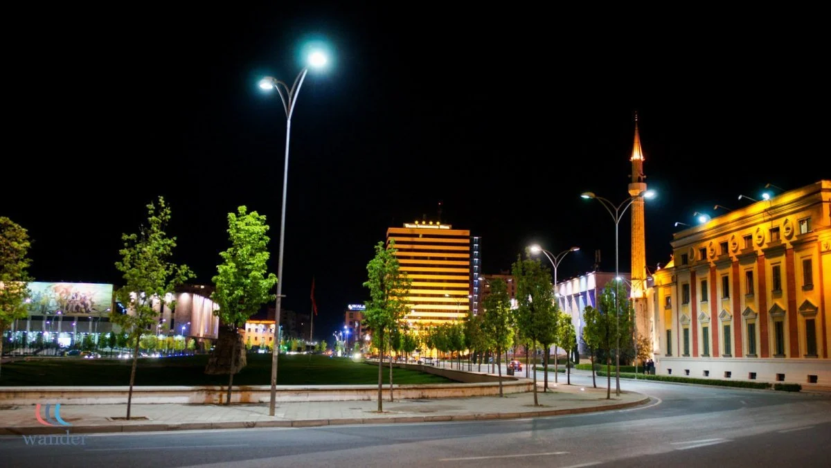 Night view of a city street with trees, lit buildings, and streetlights.