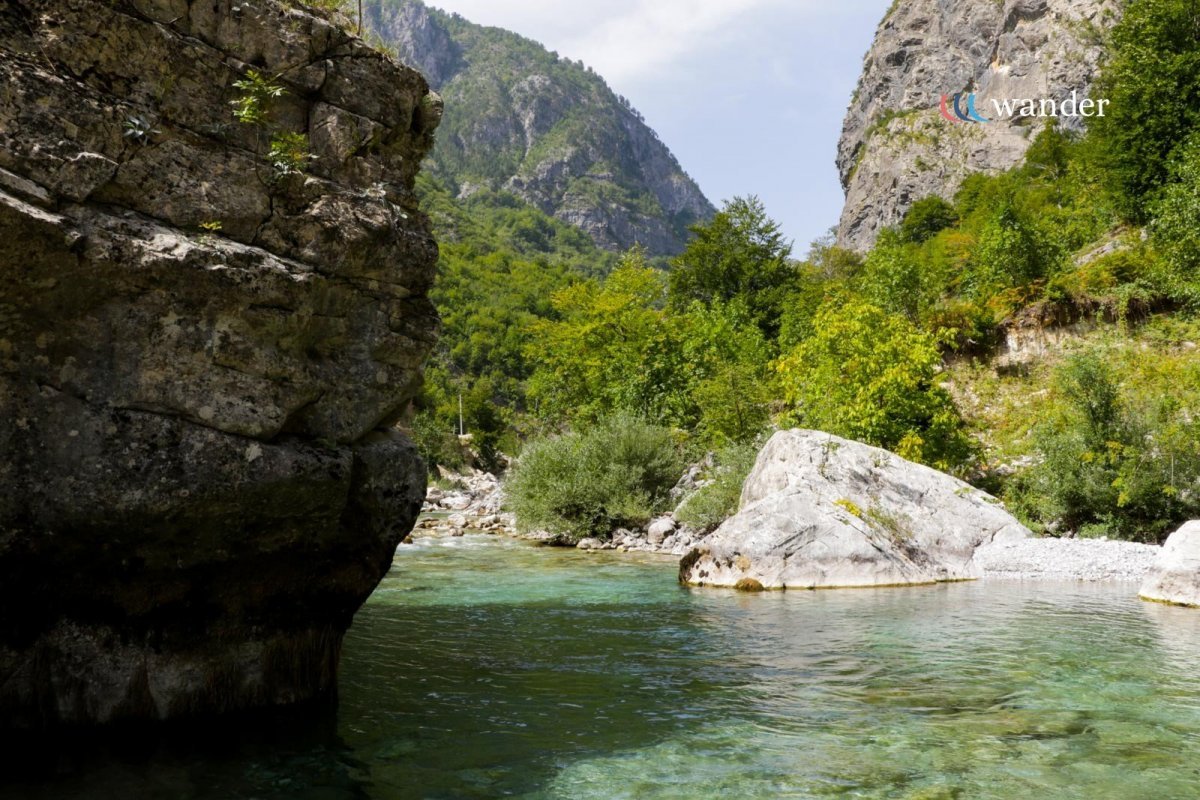 A river running through a rocky canyon with lush green trees and mountains in the background.