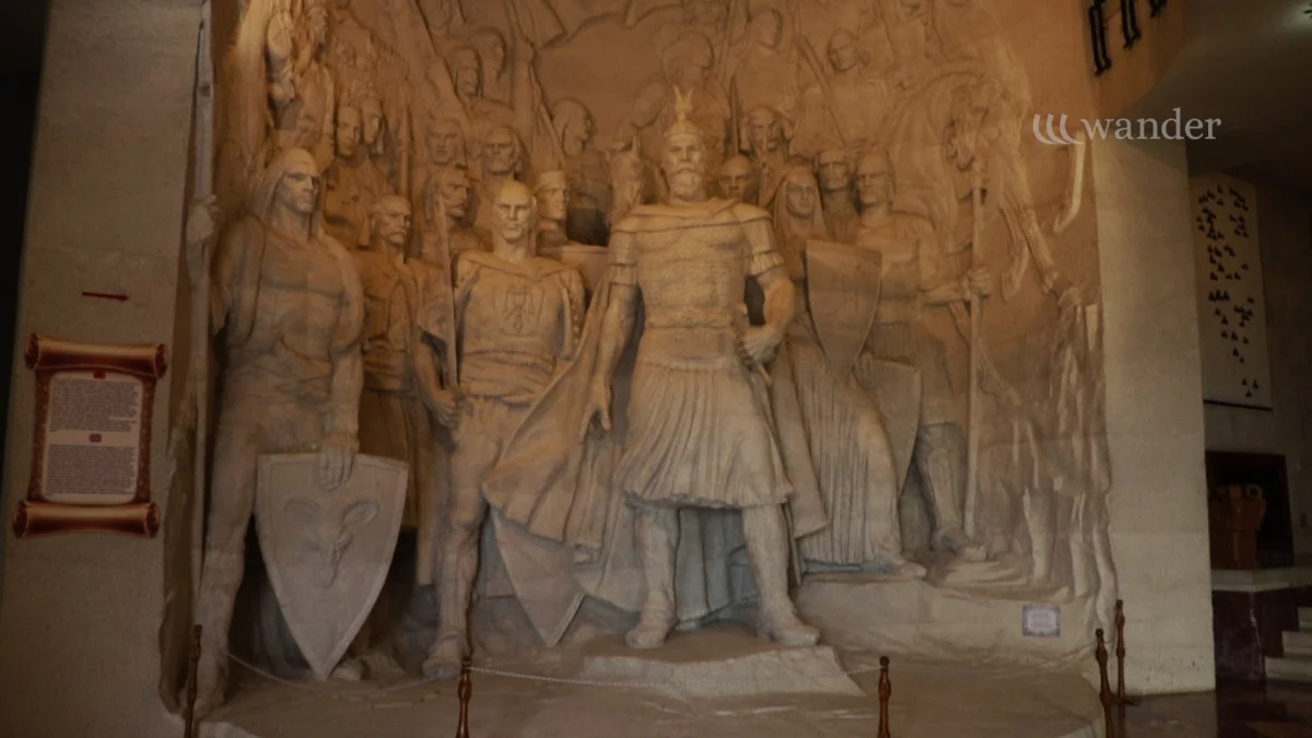 A detailed stone sculpture depicting a group of Roman soldiers and a central figure in roman attire with a staff, in a museum setting.