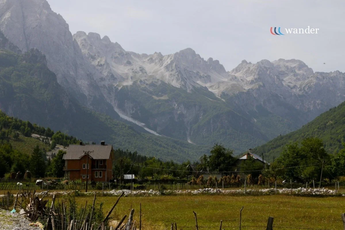 A small house in a green field with mountains in the background, under a cloudy sky.