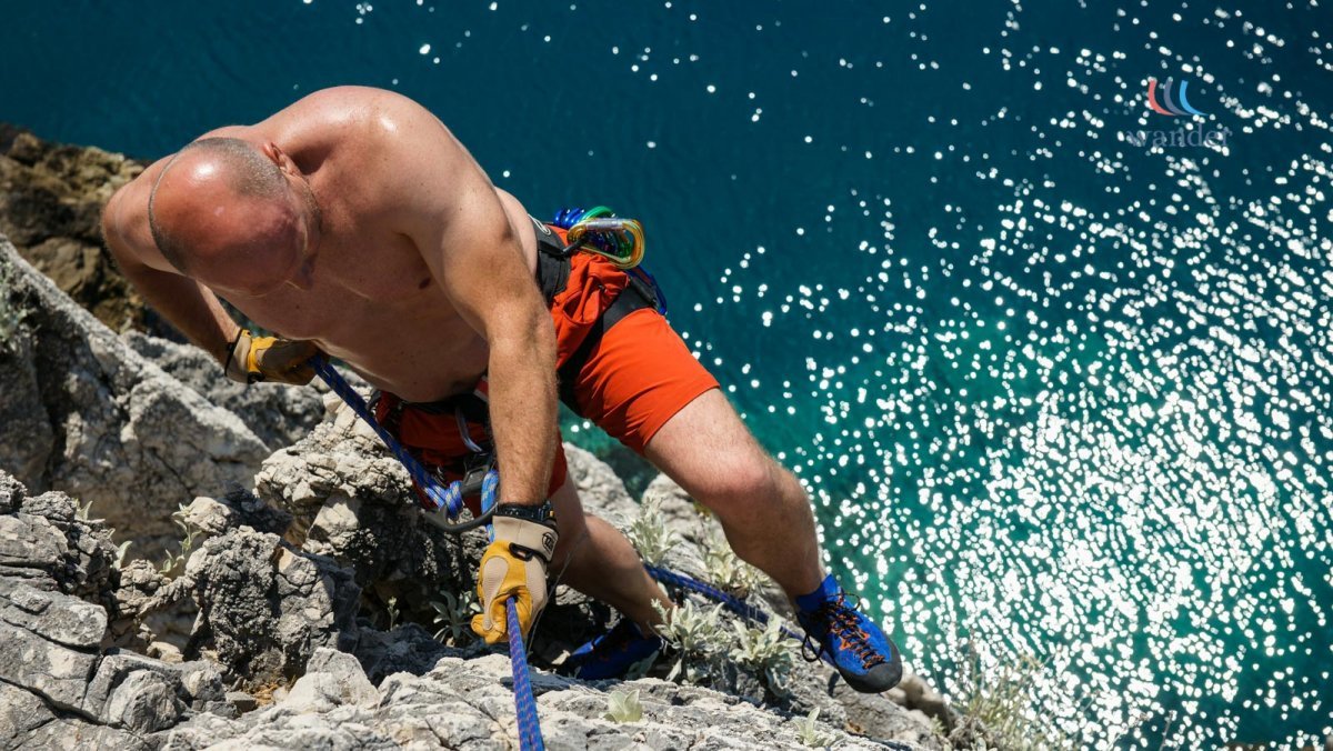 Man rock climbing on a steep cliff above water during daytime