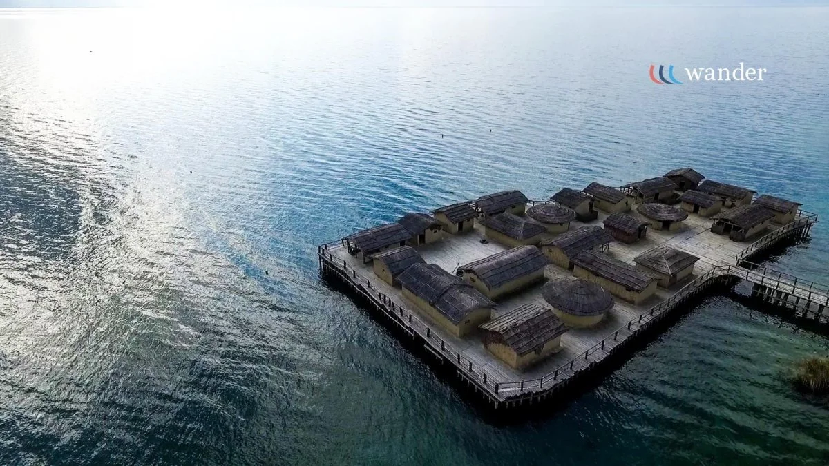 Residential houses built on a pier extending over a large body of water, with calm waves and reflections.