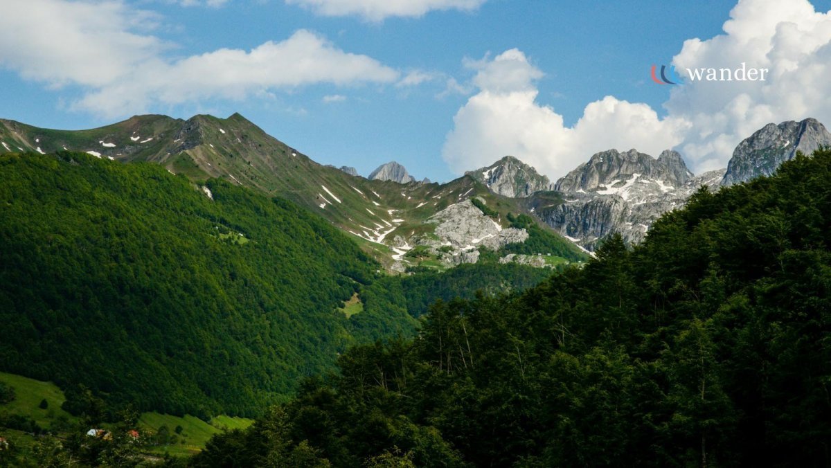 Scenic view of green mountain landscape with rocky peaks and blue sky with clouds.