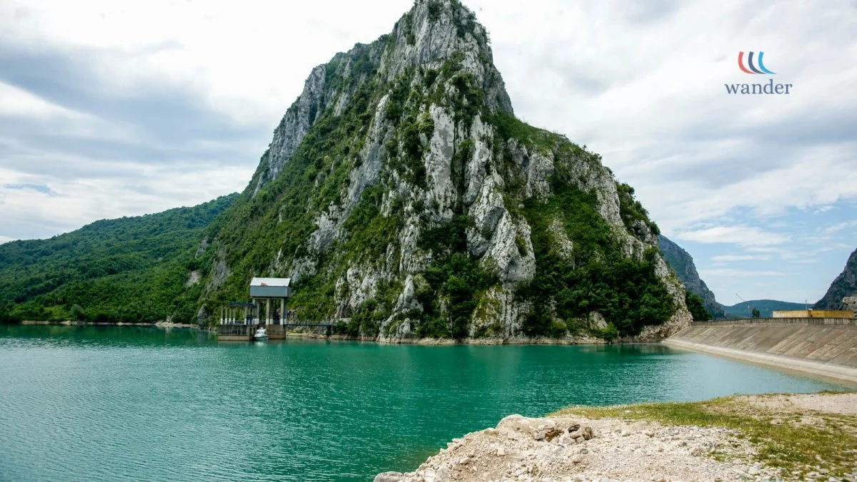 A large mountain with a rocky, green surface next to a body of water with a dam structure.