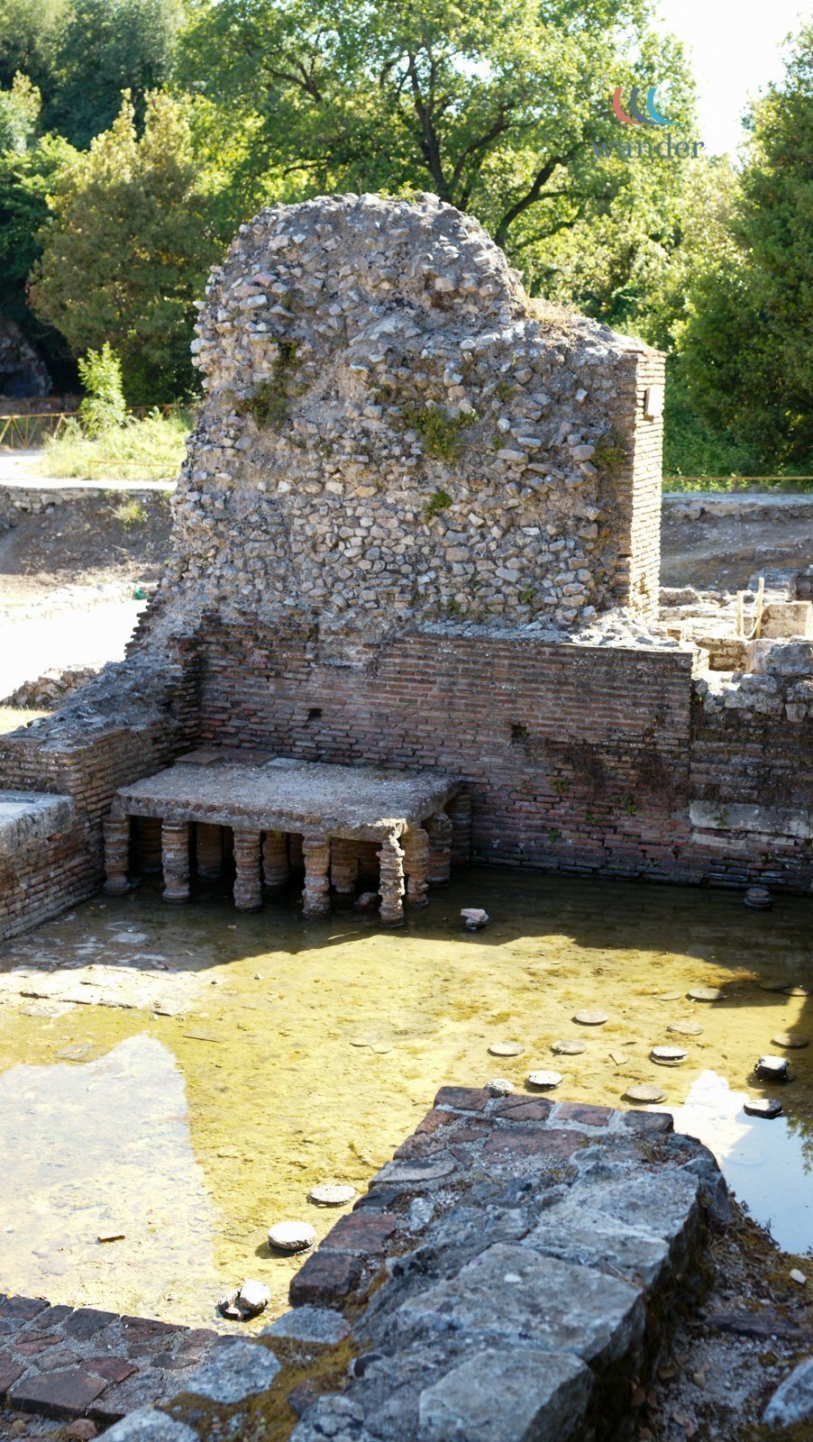 Ruins of an ancient structure with brick and stone walls, partially submerged in water, surrounded by greenery.