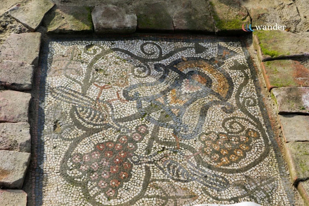 Ancient mosaic tile floor with intricate geometric and floral patterns, surrounded by stone bricks.