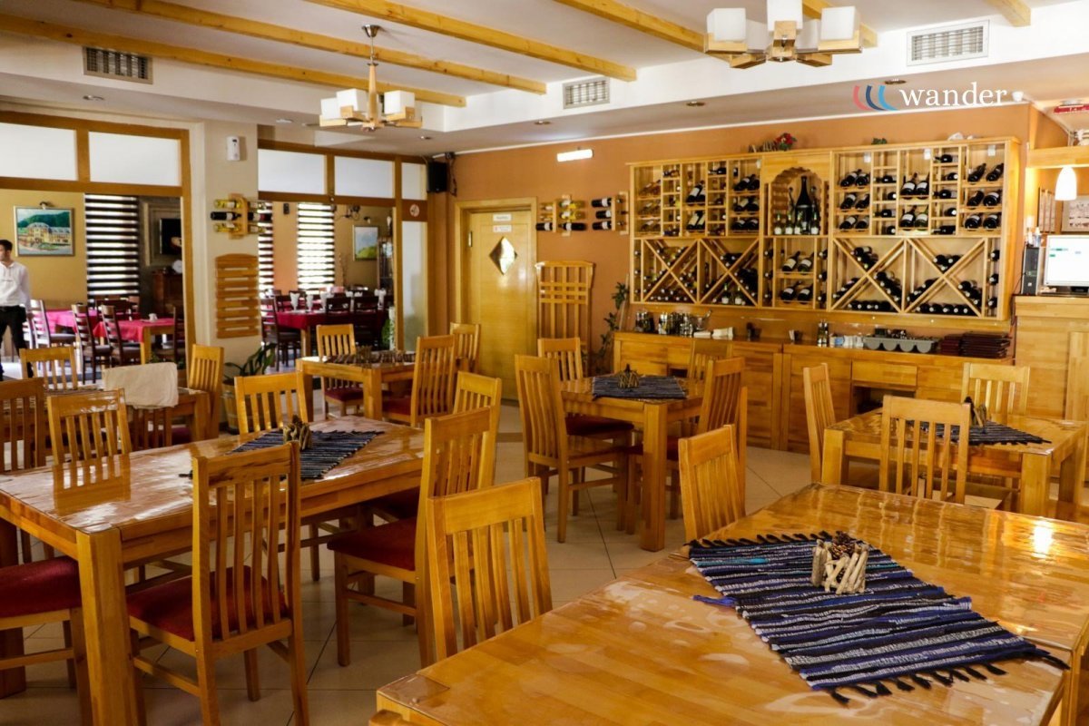 Interior of a restaurant with wooden tables and chairs, wine bottles stored in wooden racks on the wall, and a cozy cozy atmosphere.