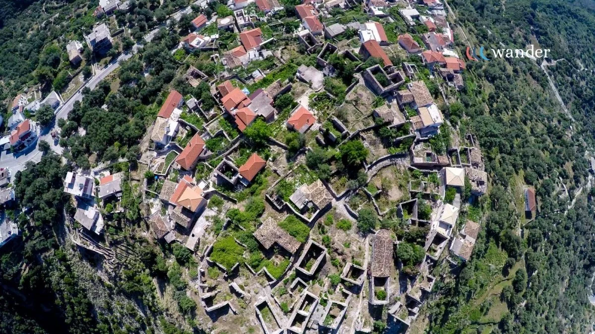 Aerial view of an ancient hillside town with stone buildings and narrow winding streets surrounded by greenery.