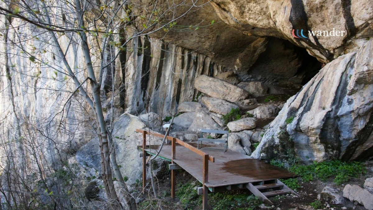 A wooden platform with a bench situated on a rocky hillside partially covered by a large overhanging rock formation.
