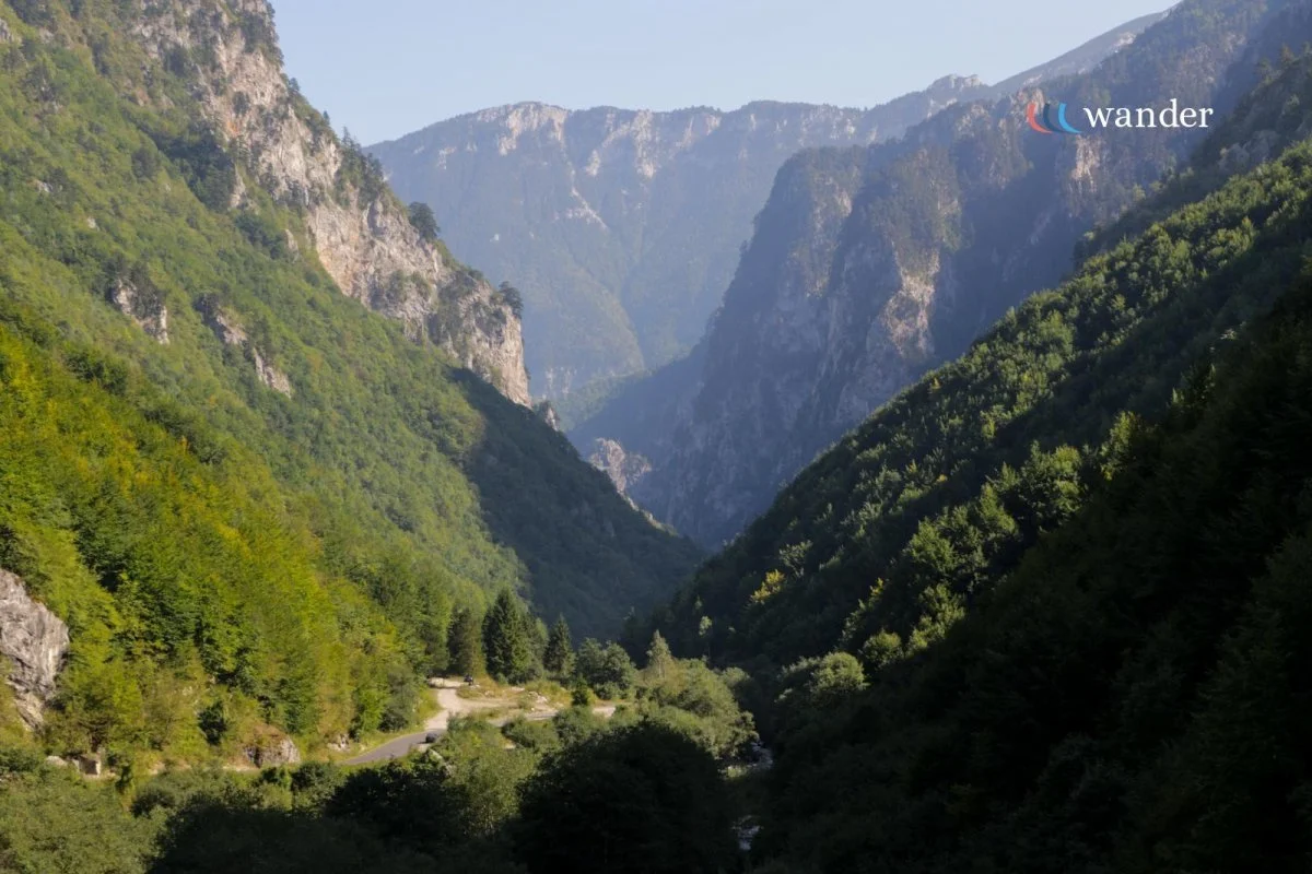 A scenic view of a green mountain valley with tall rugged mountains in the background under a clear sky.