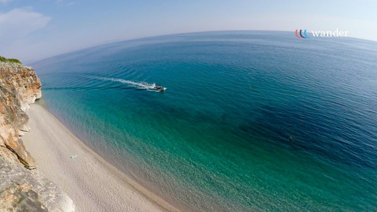 A boat sailing in clear blue ocean water near a sandy beach with rocky cliffs.