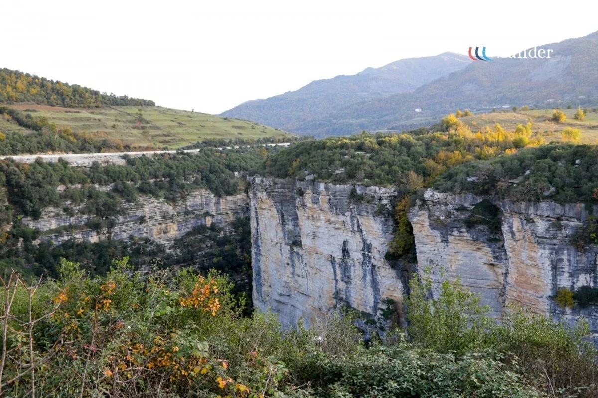 A scenic view of a canyon with tall white rock cliffs, surrounded by green vegetation and distant mountains in the background.