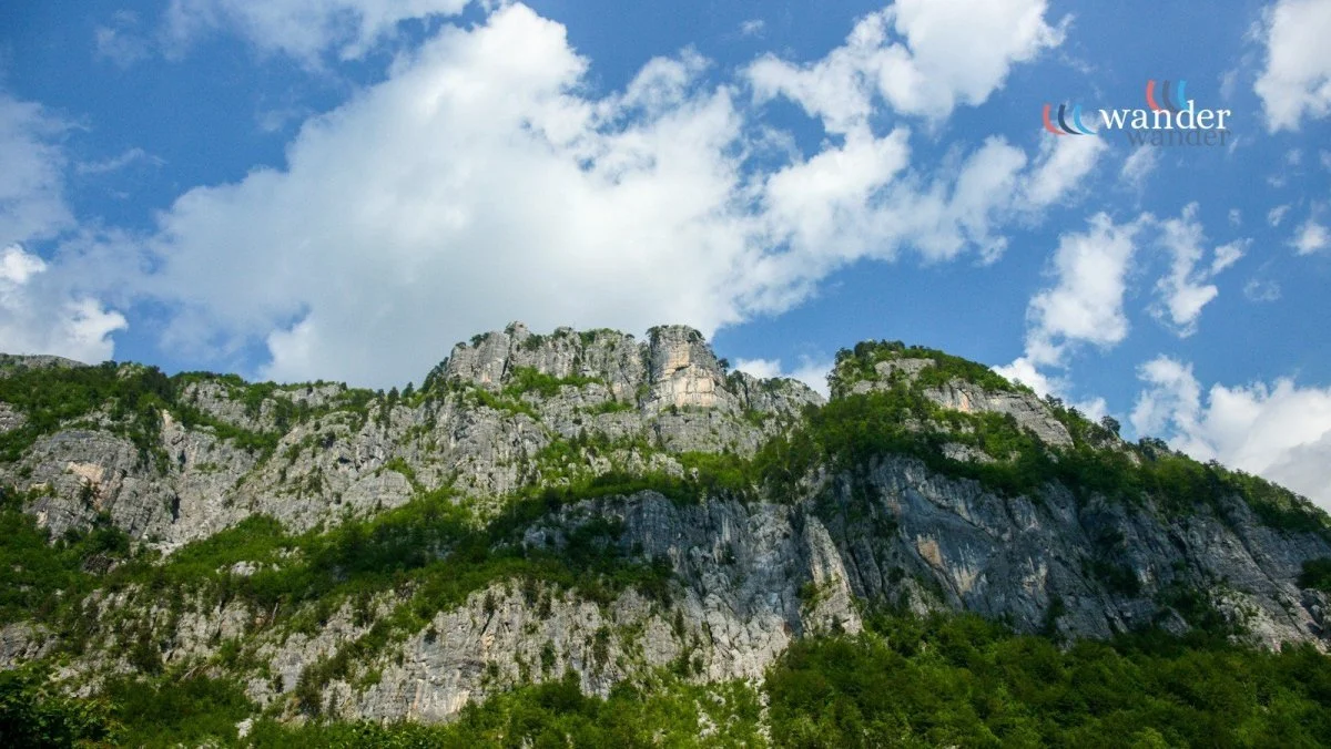 Rocky mountain with greenery and a partly cloudy sky.