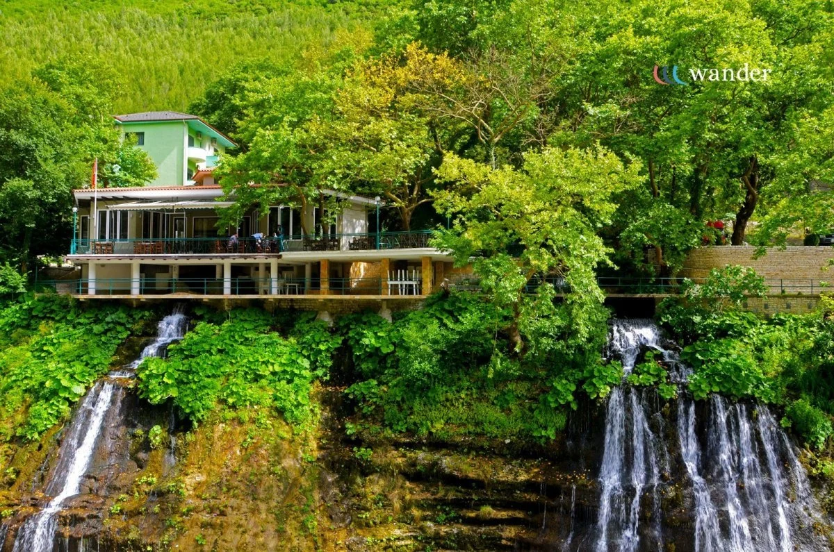 A house built on a hillside surrounded by lush green trees and plants, with waterfalls flowing below the house.