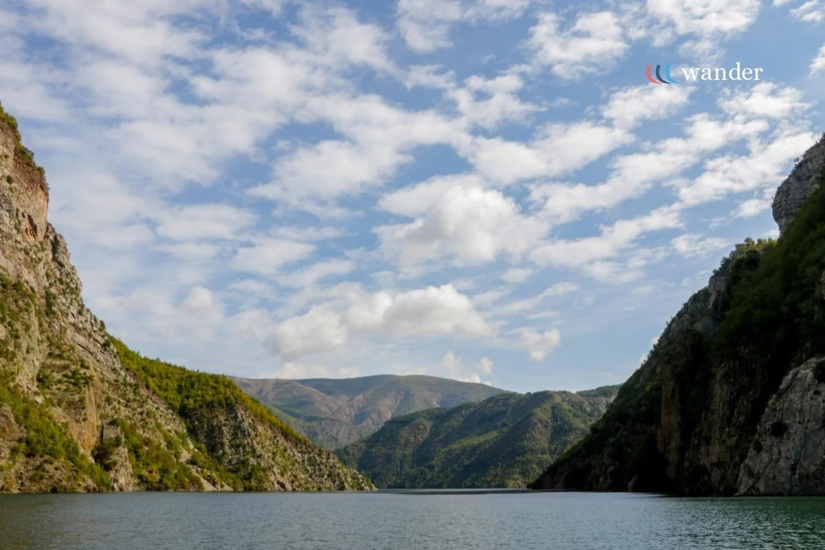 A scenic view of a river between green mountains with a partly cloudy sky.
